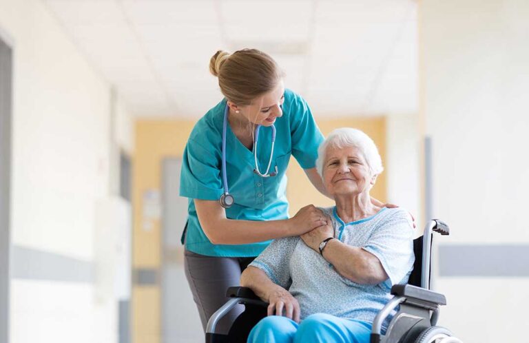A resident sitting with a staff member, both reviewing a medication organizer together at a dining table.